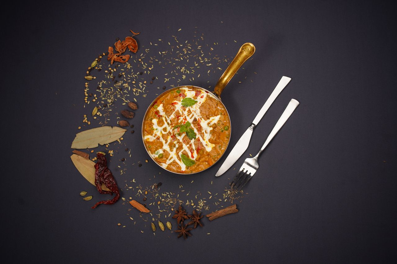 Flat lay of Indian curry in pot with spices on black background, showcasing traditional cuisine.