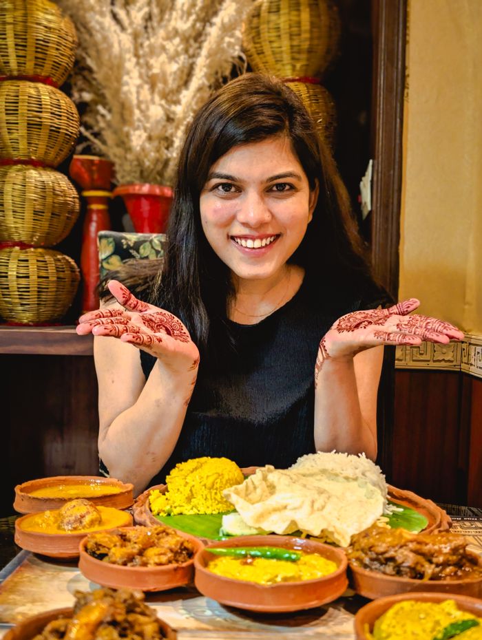 Woman with henna hands enjoying a traditional Indian thali meal in Kolkata restaurant.
